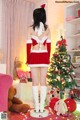 A woman in a santa outfit standing in front of a Christmas tree.